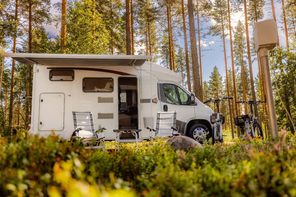 RV parked in a pine forest with camp chairs and bikes — a peaceful mobile setup ready for adventure