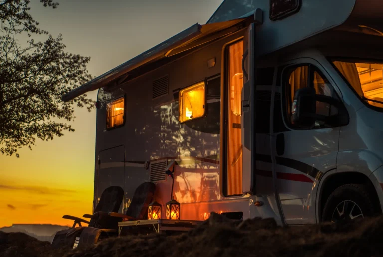 Cozy RV campsite at sunset with warm lighting, outdoor chairs, and lanterns under an awning